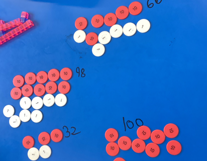 Place value counters on a blue table with the numbers they represent written next to them.